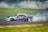 A racing car performing a drift on a track with smoke billowing from the rear tires. The car displays vibrant graphics, including the words 'MIDNIGHT' along the side. The background features a crowd of spectators blurred by the smoke.