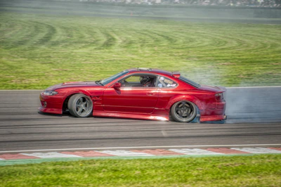 A motorsports racetrack scene with a red muscle car speeding through a curve, tire smoke rising in the background.