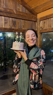 A happy customer holding a beautifully boxed shamzcapa cake, smiling warmly in a cozy kitchen setting.