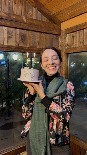 A joyful person holding a beautifully decorated cake in a bright, welcoming kitchen.
