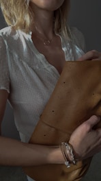 Hand holding a cream-colored beaded crossbody bag with delicate gold details