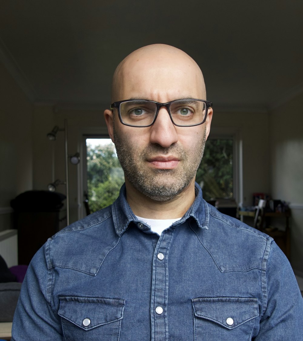 Ein glatzköpfiger Mann mit Brille, der in einem Wohnzimmer steht