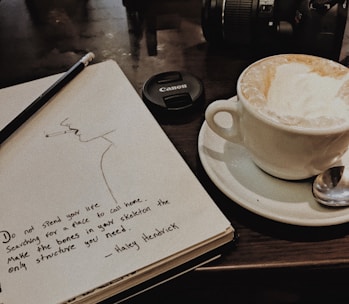 a cup of coffee next to a notebook with a drawing on it