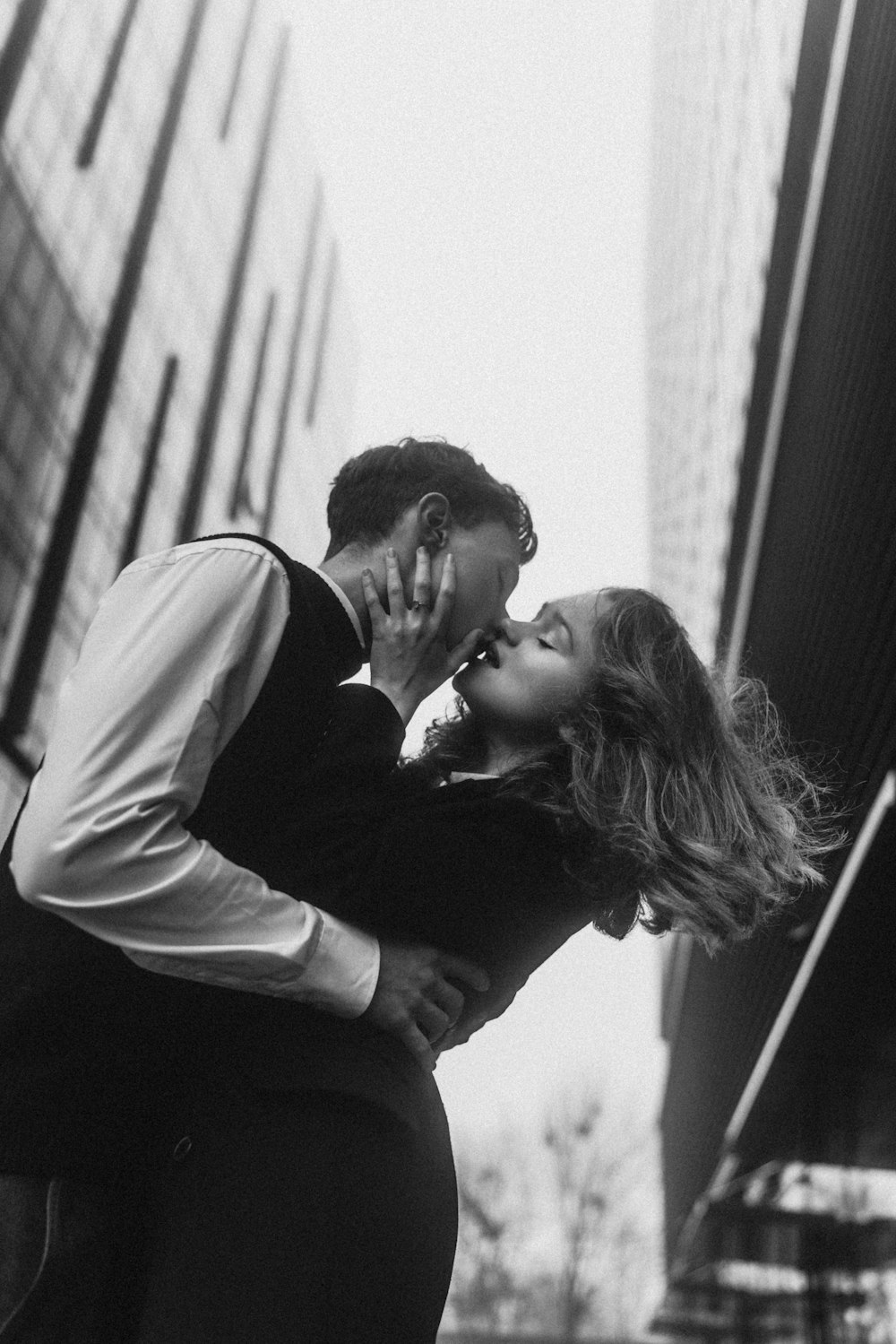 a man and a woman kissing in front of tall buildings