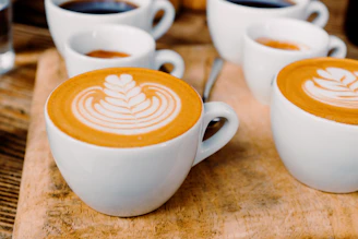 Overhead shot of a rustic wooden table featuring six different coffee drinks in elegant cups, highlighting rich browns and creamy textures.