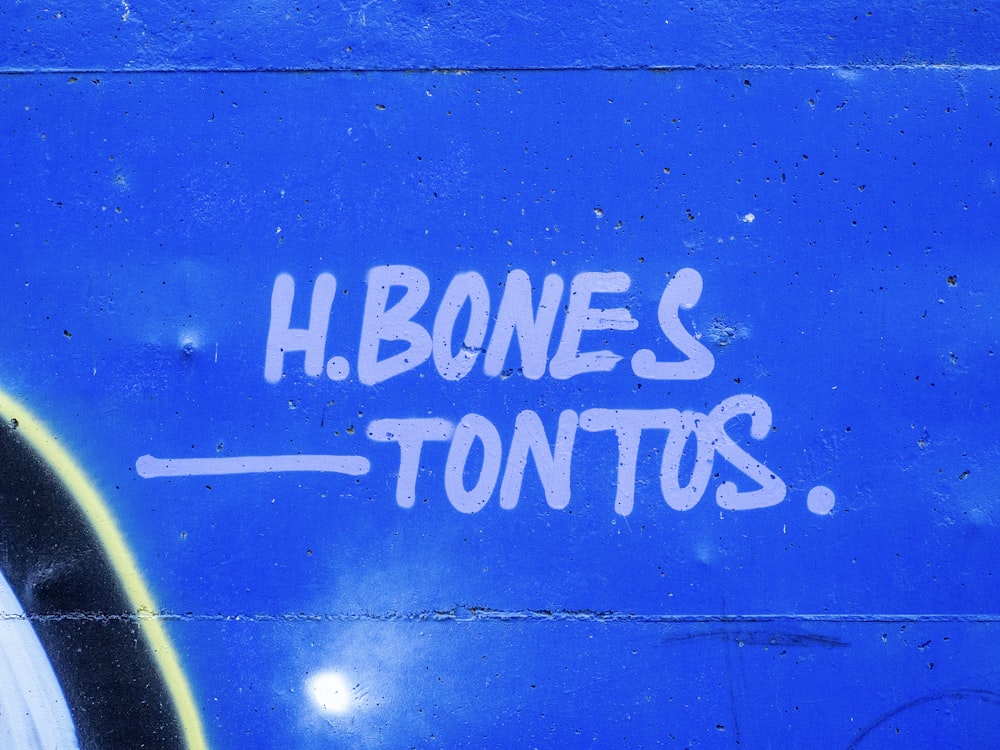 Graffiti en el costado de una pared azul que dice H Bones Tons