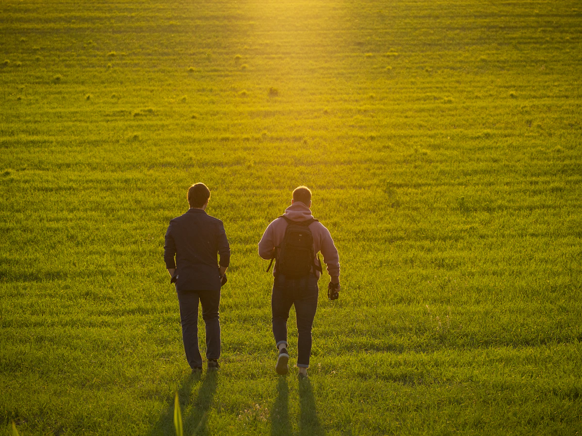 Zwei Menschen gehen bei tief stehender Sonne über ein grünes Feld