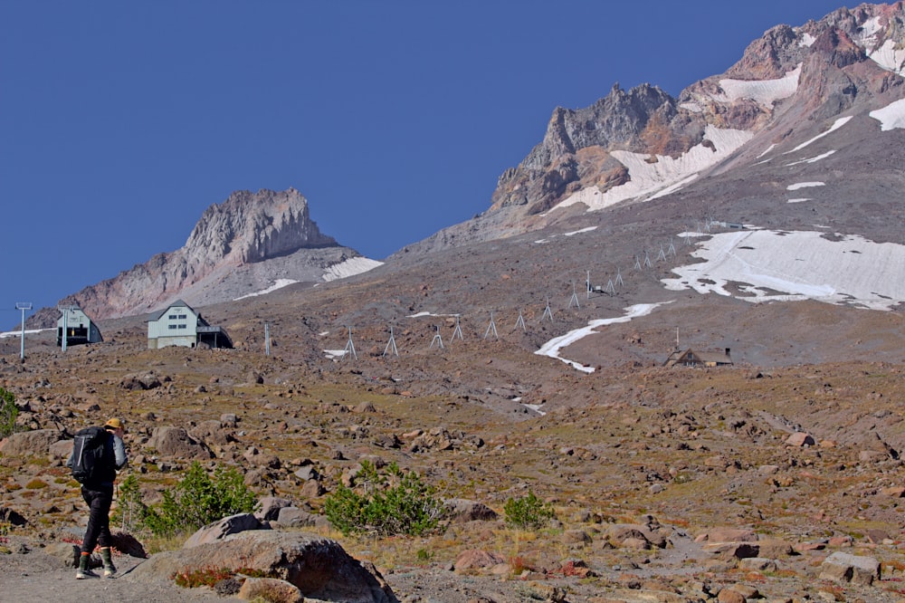 Un hombre subiendo una montaña con una casa al fondo