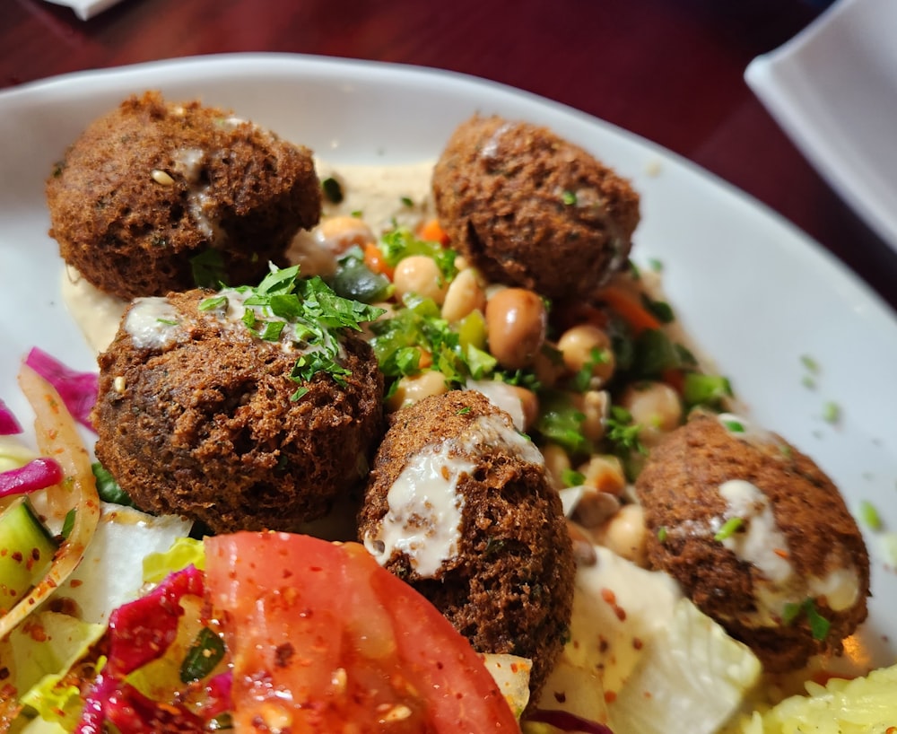 un plato blanco cubierto con albóndigas y una ensalada