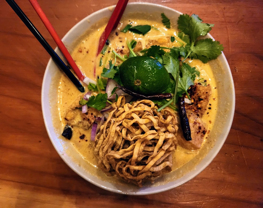 a bowl of noodles and vegetables with chopsticks