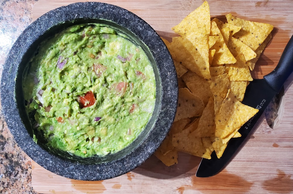 a bowl of guacamole next to a bowl of tortilla chips