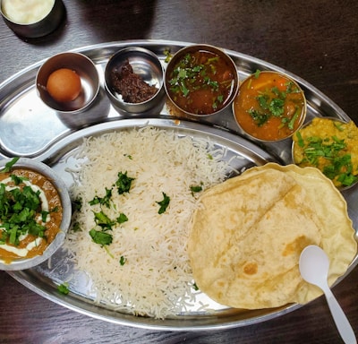 a silver plate topped with rice and different types of food