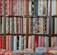 A colorful assortment of fabric rolls neatly arranged on wooden shelves. The fabrics feature various patterns and designs, including floral, geometric, and abstract motifs, with a wide range of colors from vibrant reds and blues to soft pastels. Each roll is tightly coiled, showcasing the diversity and richness of textures and styles.