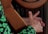 A person's hand is placed on the strings of a wooden harp, with fingers poised to pluck or strum. The natural grain of the wood and the delicate strings are visible, highlighting the craftsmanship of the instrument. The person is wearing a dark garment with bright green clover patterns.