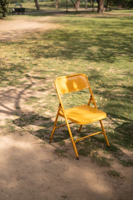 Yellow folding chair sitting alone in dappled sunlight on grass in a quiet park