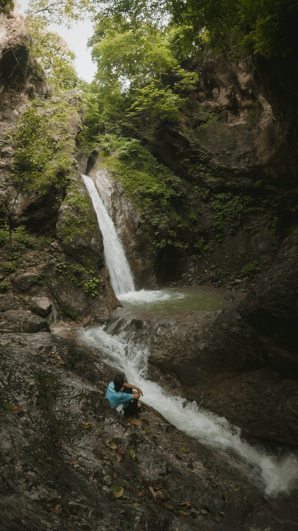 a person sitting on a rock next to a waterfall