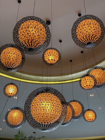 Hanging spherical pendant lights with intricate geometric wire designs surround warm glowing bulbs. These lights are suspended from a curved ceiling with recessed lighting, creating an elegant and cozy ambiance.