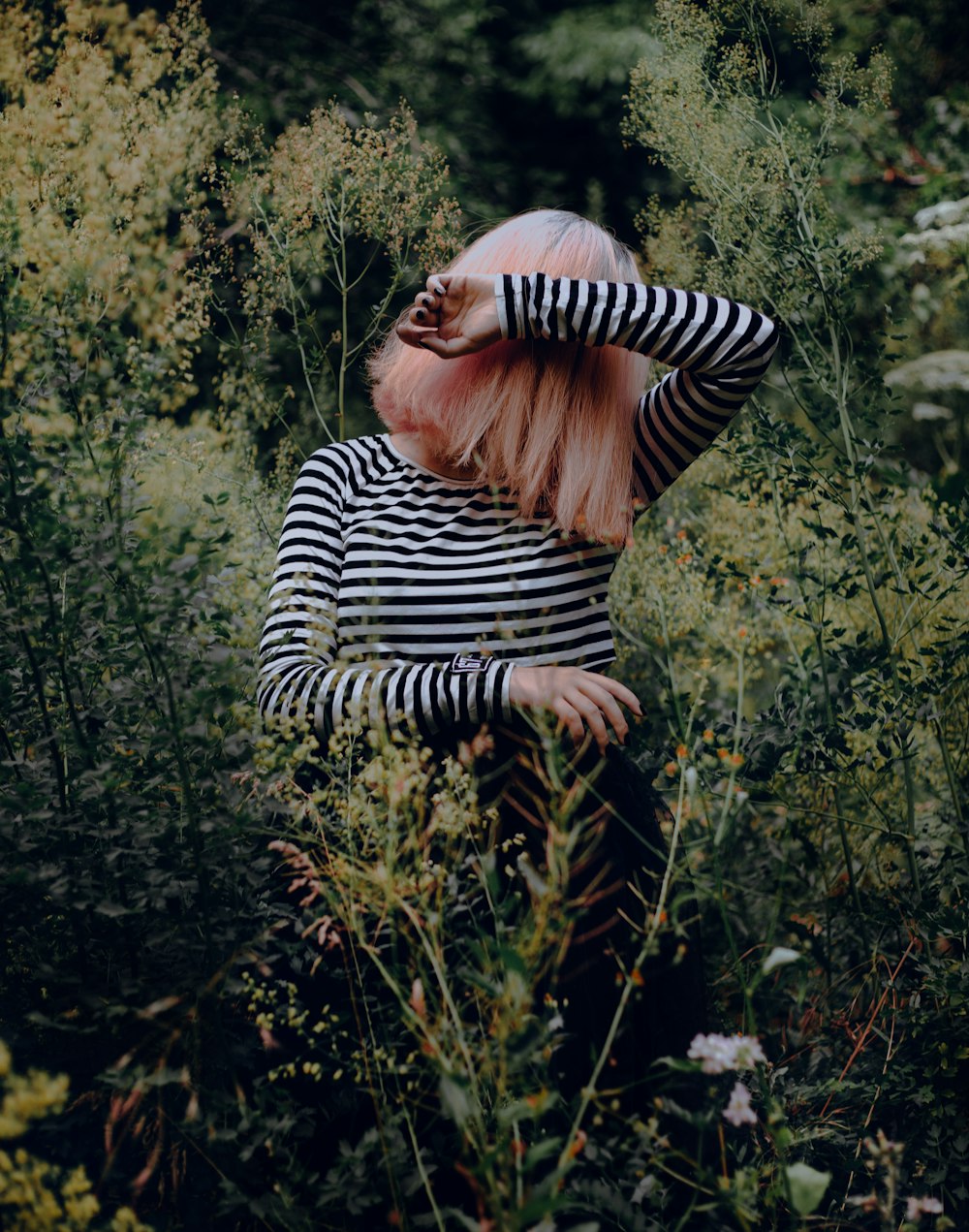 a woman with pink hair standing in tall grass