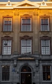 A grand building with classical architectural elements, featuring large, symmetrical windows and detailed stonework. The facade includes Roman numerals 'ANNO MCMX' and the name 'Dutch Golden Hotel' above the entrance. A warm, golden light illuminates the upper portion.