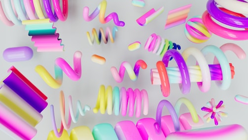 A collection of vibrant, multicolored abstract shapes and spirals against a light backdrop, featuring smooth, shiny surfaces and a playful arrangement. The scene is dynamic and visually stimulating with a variety of forms like coils, curls, and rectangles.