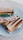 A toasted sandwich placed on a white plate, featuring layers of neatly stacked grilled bread filled with lettuce, slices of meat, and melted cheese. The grill marks are distinct across the top slice of bread, and the contents spill slightly over the sides.