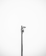 A minimalistic image featuring a single security camera mounted on a tall metal pole against a plain white background. The setup is centralized and the black and white color scheme adds a stark contrast, emphasizing the industrial design of the camera.