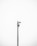 A minimalistic image featuring a single security camera mounted on a tall metal pole against a plain white background. The setup is centralized and the black and white color scheme adds a stark contrast, emphasizing the industrial design of the camera.