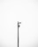 A minimalistic image featuring a single security camera mounted on a tall metal pole against a plain white background. The setup is centralized and the black and white color scheme adds a stark contrast, emphasizing the industrial design of the camera.