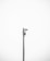 A minimalistic image featuring a single security camera mounted on a tall metal pole against a plain white background. The setup is centralized and the black and white color scheme adds a stark contrast, emphasizing the industrial design of the camera.
