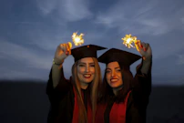 A lively graduation scene with smiling graduates in caps and gowns celebrating outdoors.