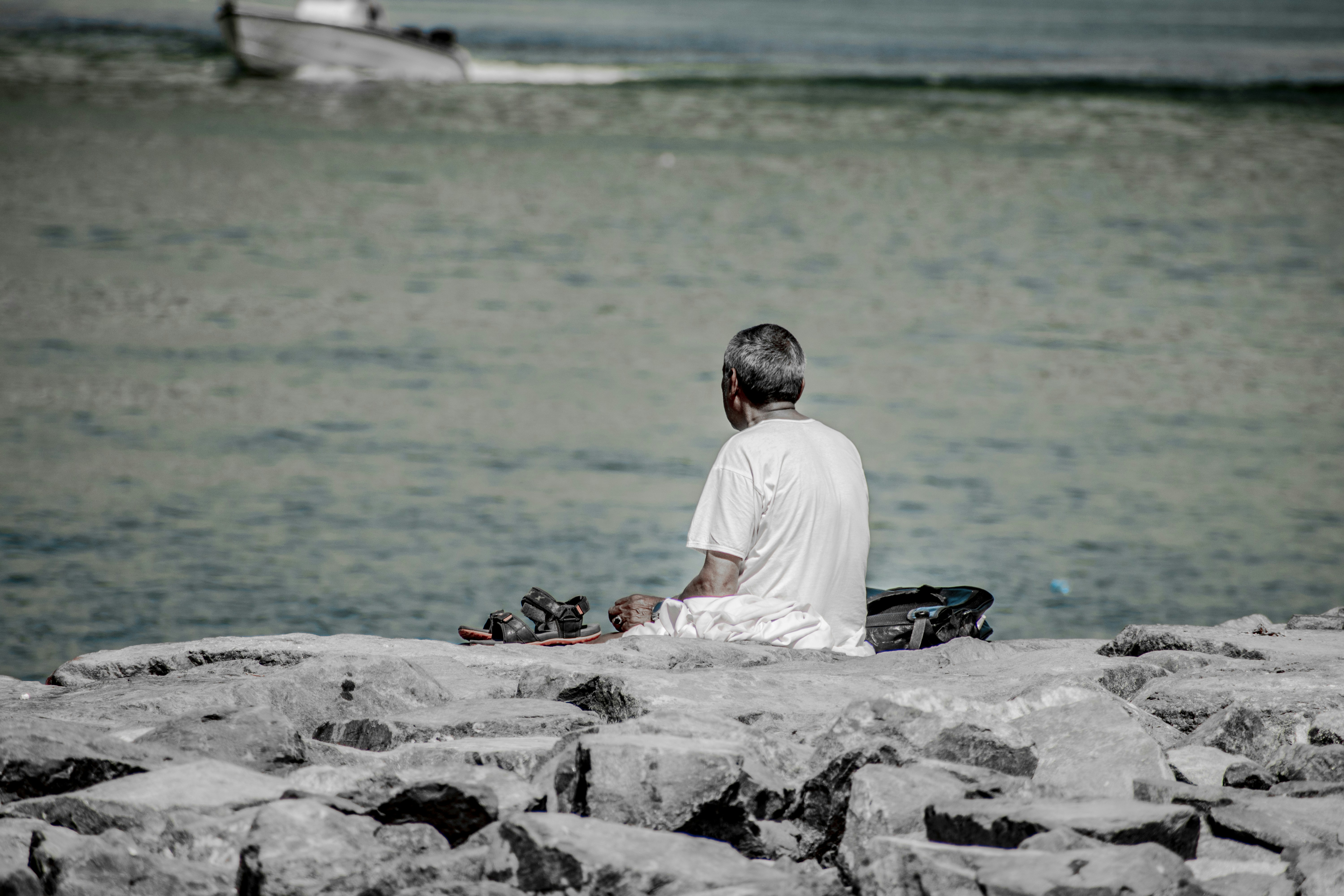 a man sitting on a rock next to a body of water