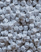A large pile of white dice is scattered, each with black dots representing the numbers one through six. The dice are tightly packed together, creating a sense of randomness and abundance.