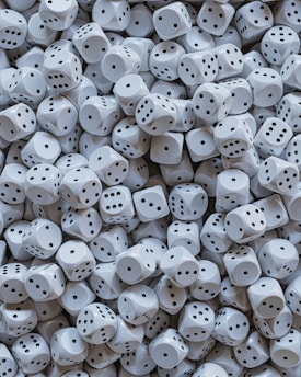 A large pile of white dice is scattered, each with black dots representing the numbers one through six. The dice are tightly packed together, creating a sense of randomness and abundance.