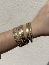 A wrist adorned with several gold bangles, each featuring a variety of engraved symbols and embedded stones, giving a luxurious and elegant appearance.