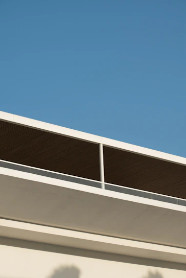 A sleek, modern outdoor patio structure with clean lines and minimalist design, set against a bright blue sky.