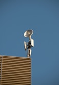 A satellite dish and antenna mounted on the corner of a modern building with slatted panels, set against a clear blue sky.