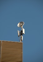 A satellite dish and antenna mounted on the corner of a modern building with slatted panels, set against a clear blue sky.