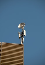 TV antenna and satellite dish installed on a rooftop against a clear blue sky.
