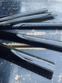 Several strips of developed film negatives are laid out on a textured, weathered surface. The shiny black film has visible sprocket holes along the edges, and the surface reflects light, emphasizing the glossy texture.