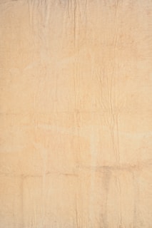 A textured beige surface with visible creases and subtle tonal variations, resembling aged or weathered parchment paper.