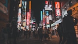 A bustling street scene in Surabaya featuring multiple neon box signs lighting up local shops at night.