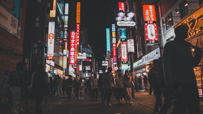 A bustling street scene in Surabaya featuring multiple neon box signs lighting up local shops at night.