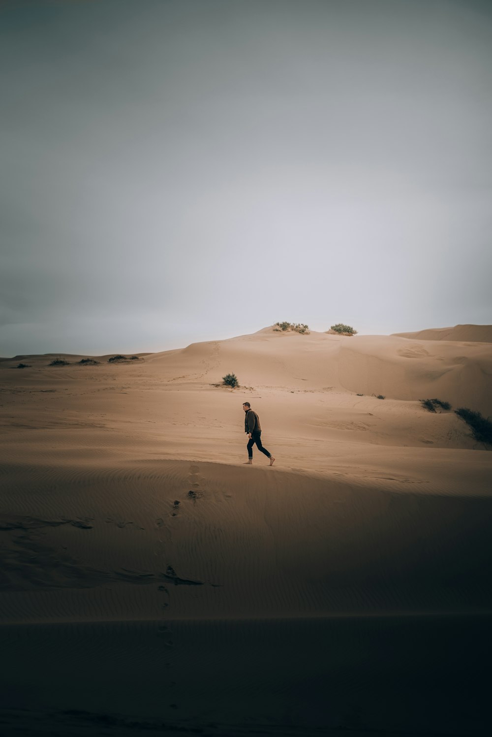 a man walking across a sandy desert under a cloudy sky