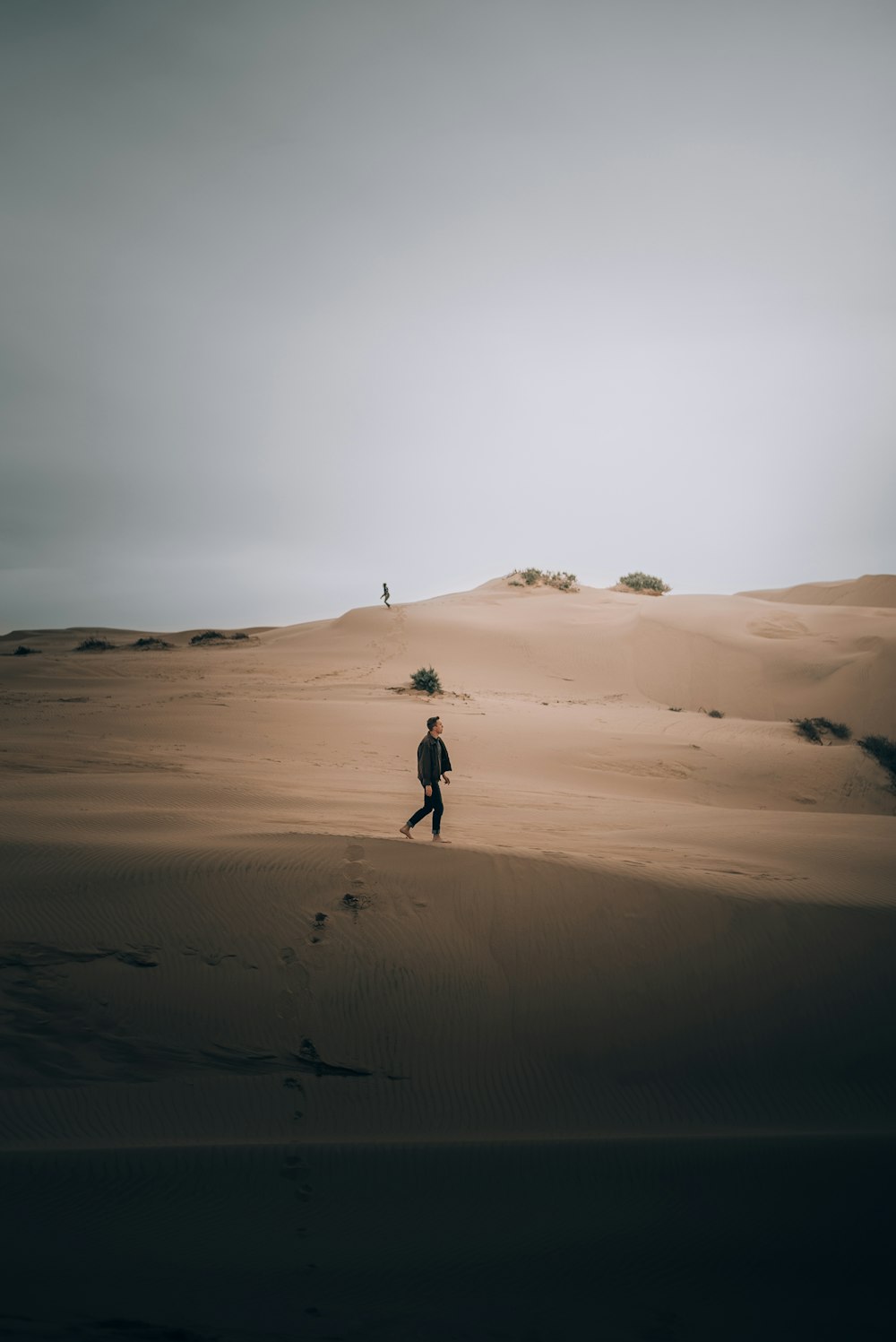 a man walking across a sandy desert under a cloudy sky