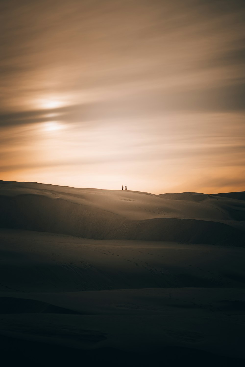 a couple of people standing on top of a sandy hill