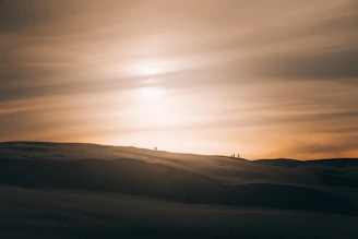 A panoramic shot of a desert sunset with a group of explorers trekking across golden dunes under a vast sky.
