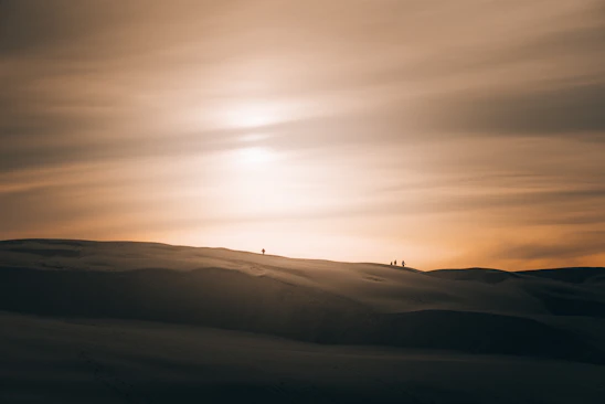 A panoramic shot of a desert sunset with a group of explorers trekking across golden dunes under a vast sky.