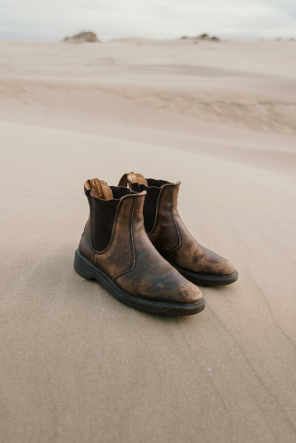a pair of brown boots sitting on top of a sandy beach