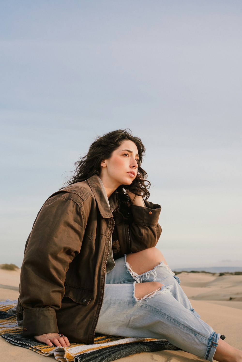 a woman sitting on top of a blanket on top of a beach