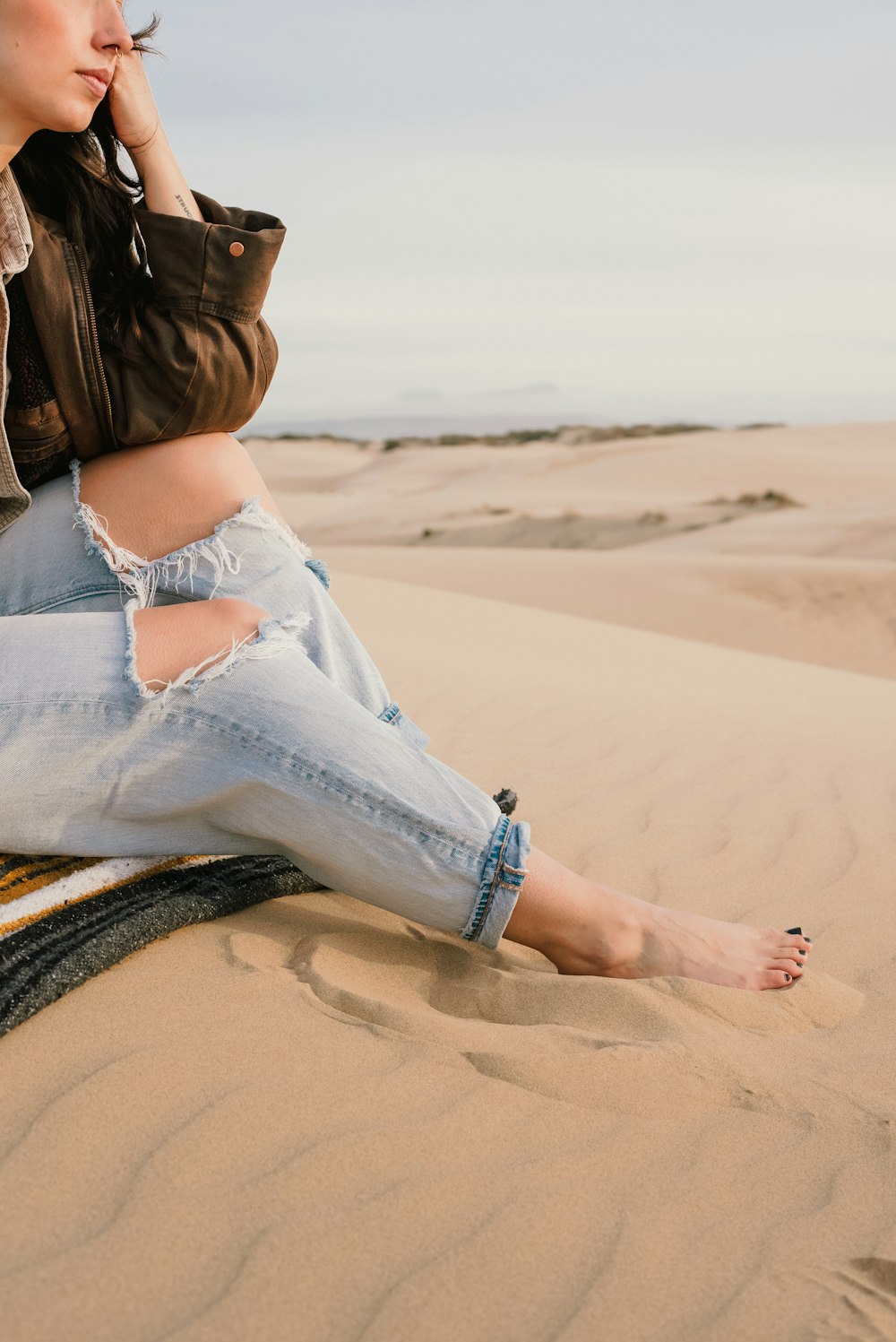 a woman sitting on top of a blanket in the sand